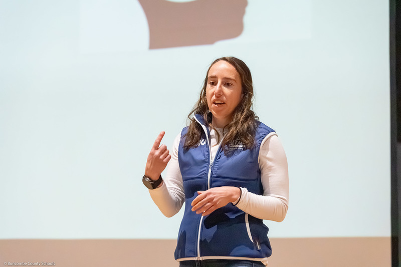 Marisa Romeo speaks on stage with a presentation slide behind her.