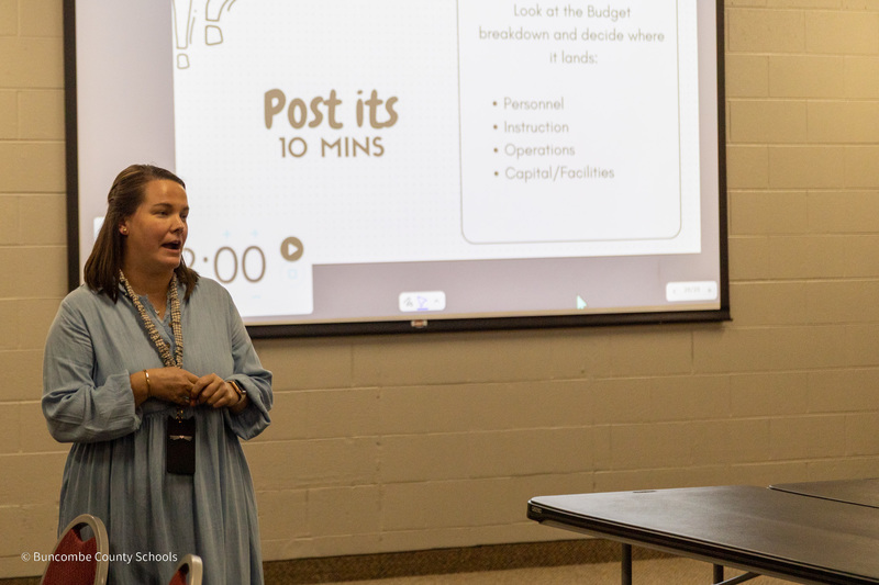 A teacher stands in front of the room speaking to the council.
