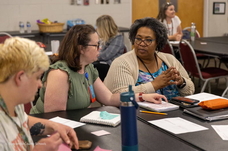 Two teachers seated talking at the council meeting.