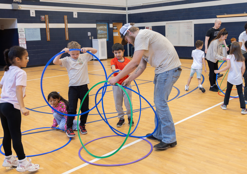 Parent helping students build a hula hoop hut