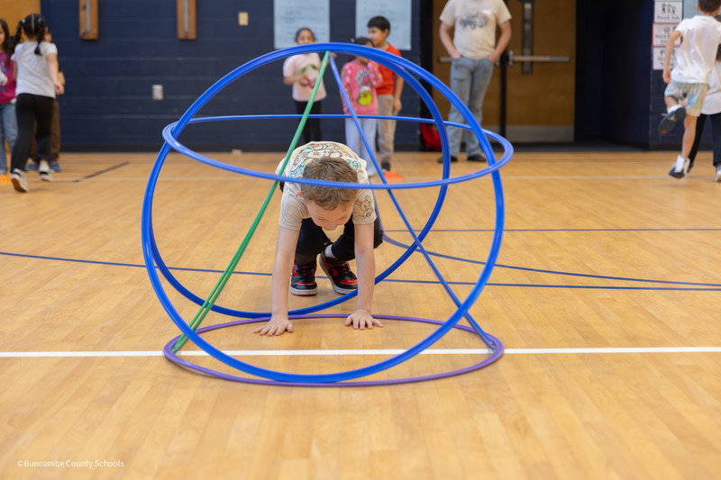 Student crawling through hula hoop hut during a relay race