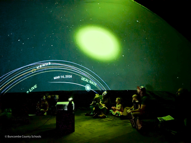 A family looks up at an image of the sun projected on an inflatable planetarium dome.