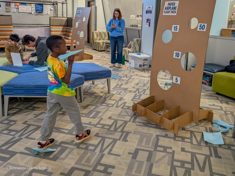 A student throws a paper airplane at a target.