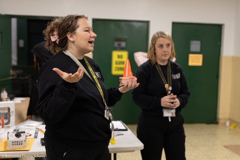 CSI expert holding up small orange cones with letters on them, and asking the students what they think the cones are used for in an investigation.