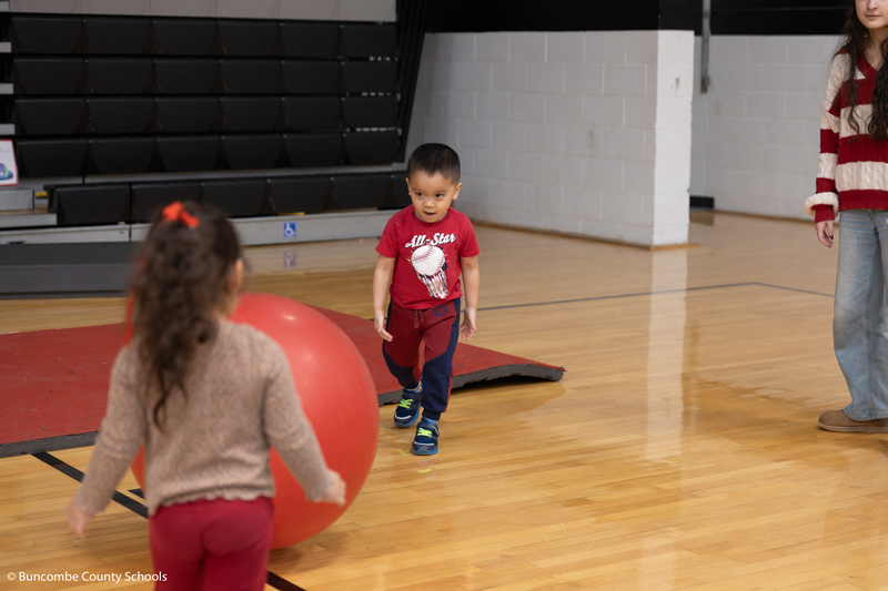 Two preschoolers kicking a large red ball back and forth. 