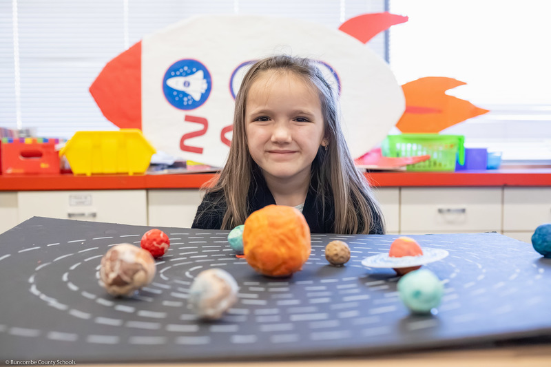 A student sits behind a homemade model of the solar system.
