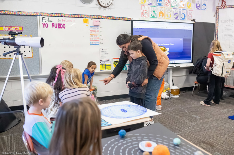 A teacher guides a student to look at another student's project.