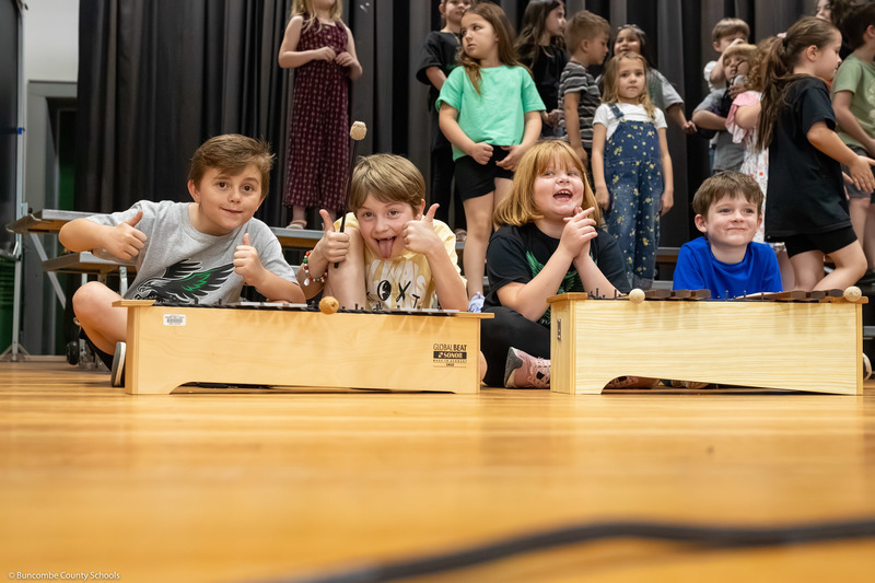 Students smile behind xylophones while waiting for a performance to begin.