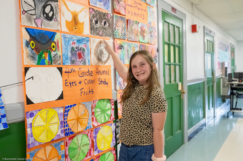 A student points to her animal eye art on a hallway wall.