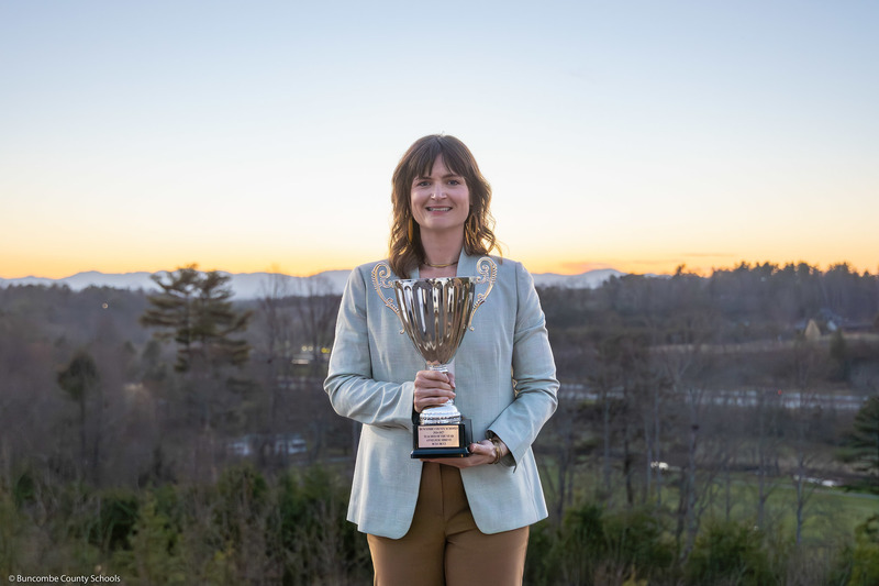 Ms. Shreve stands outside in the sunset holding her trophy.