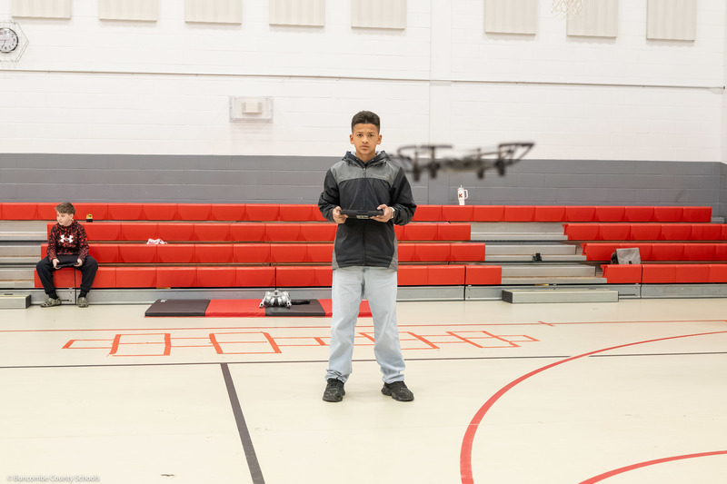 A boy operates a drone in the gym using a tablet.