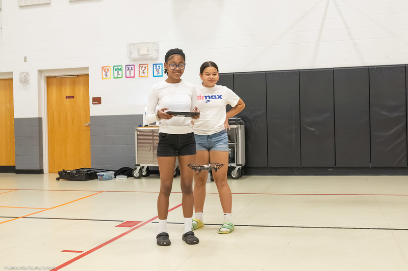 Two girls operate a drone in the gym using a tablet.