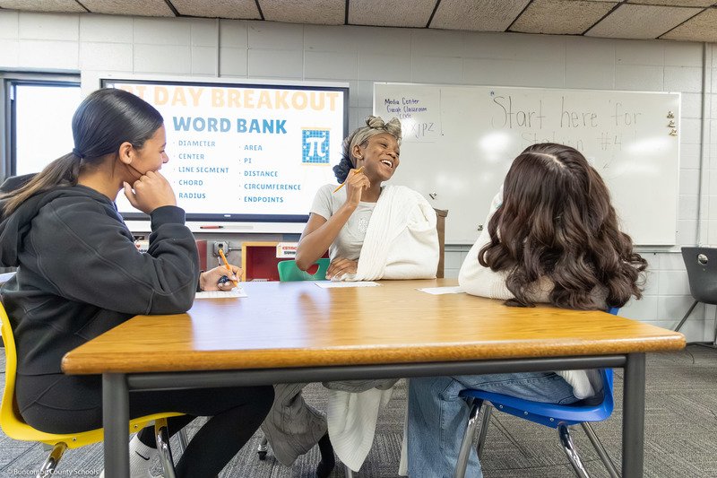 Three students laugh while working on a math problem.