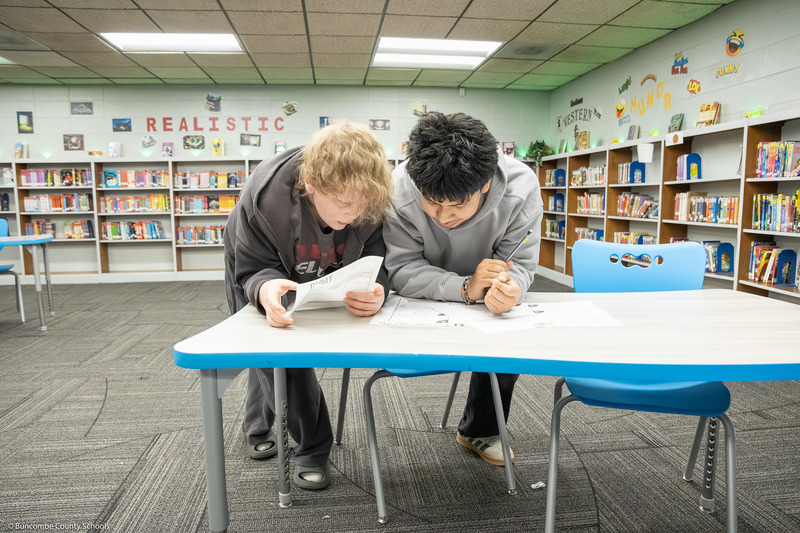 Two students lean over a table while working on a math problem.