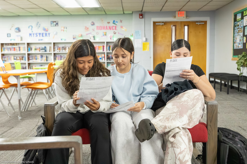 Three students sit on a couch while working on a math problem.