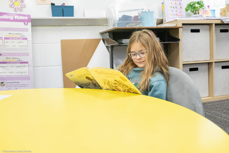 A third grade student smiles while reading a book.