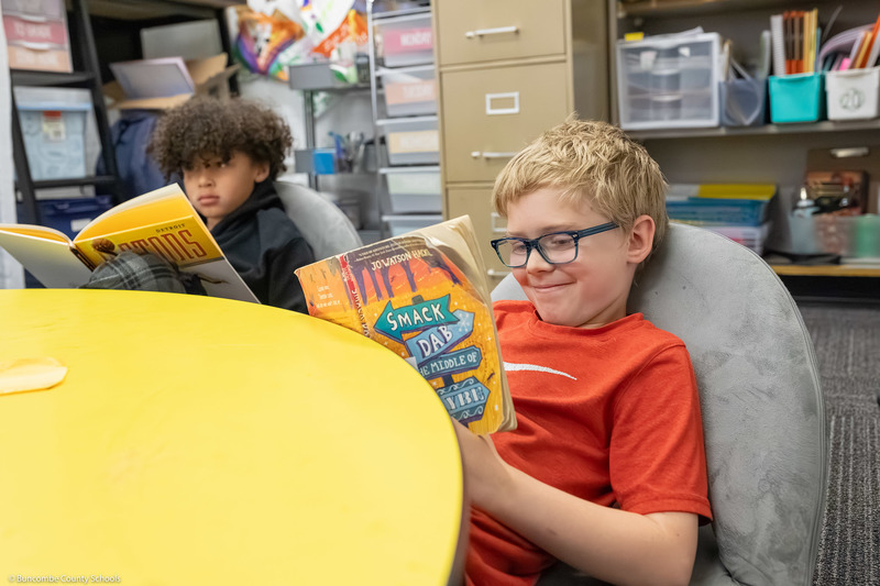 A third grade student smiles while reading a book.