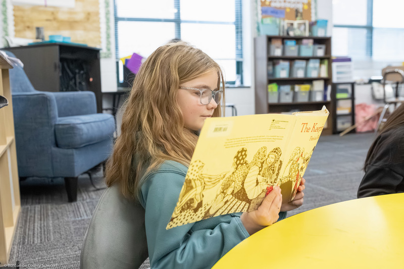 A third grade student smiles while reading a book.