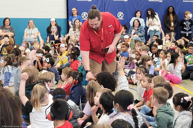 An adult hands an item to a student during a school assembly.