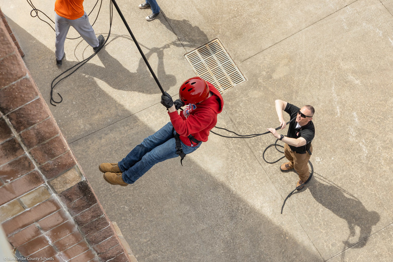 A student pushes off the wall while rappelling down the tower.