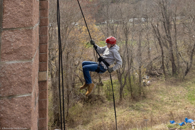 A student pushes off the wall while rappelling down the tower.