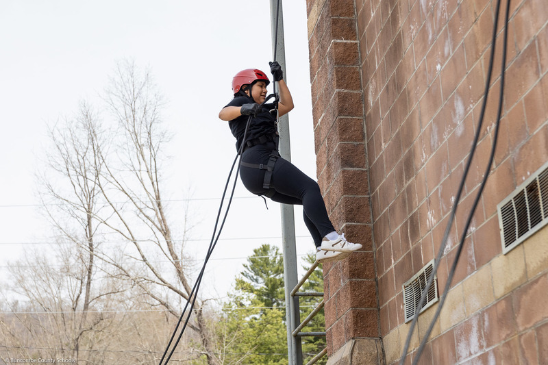A student pushes off the wall while rappelling down the tower.