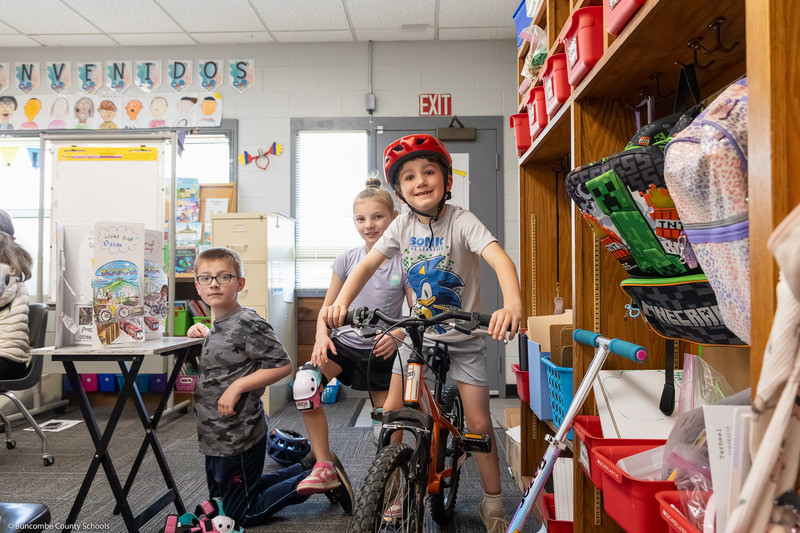 A boy smiles while sitting on a bicycle in a classroom.