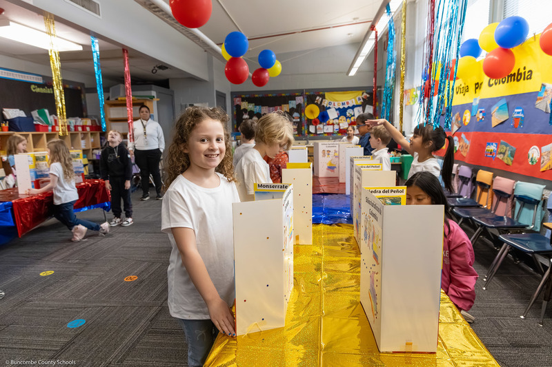 A student looks at the camera while standing next to her project in a colorfully decorated room.