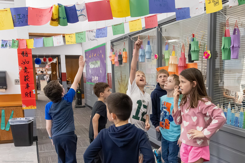 Students point upwards at colorful flags in a hallway.