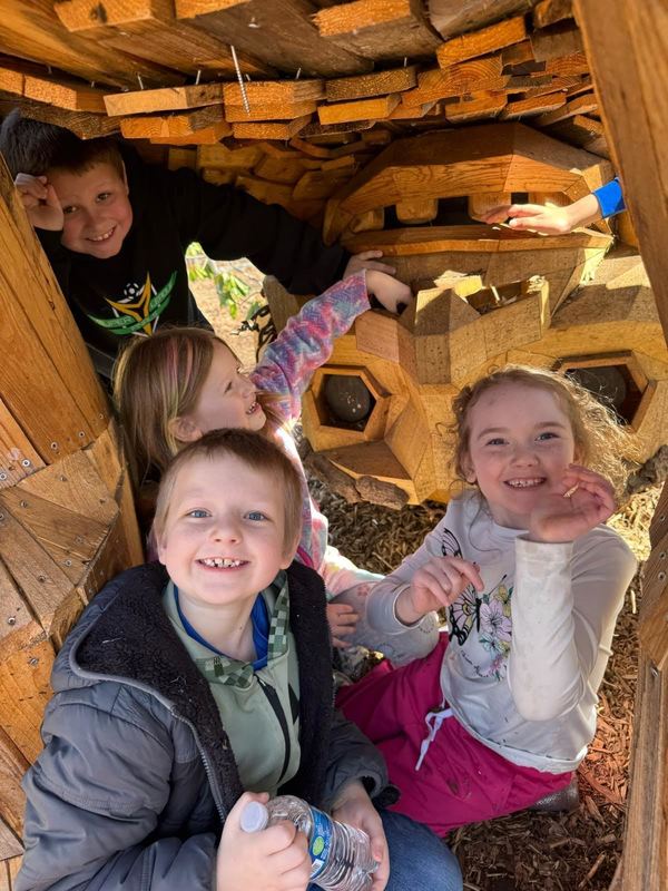 Students underneath a wooden troll, smiling at the camera. 
