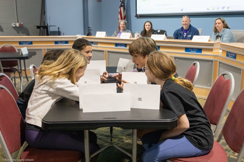 Students lean in to confer at a table during the competition.