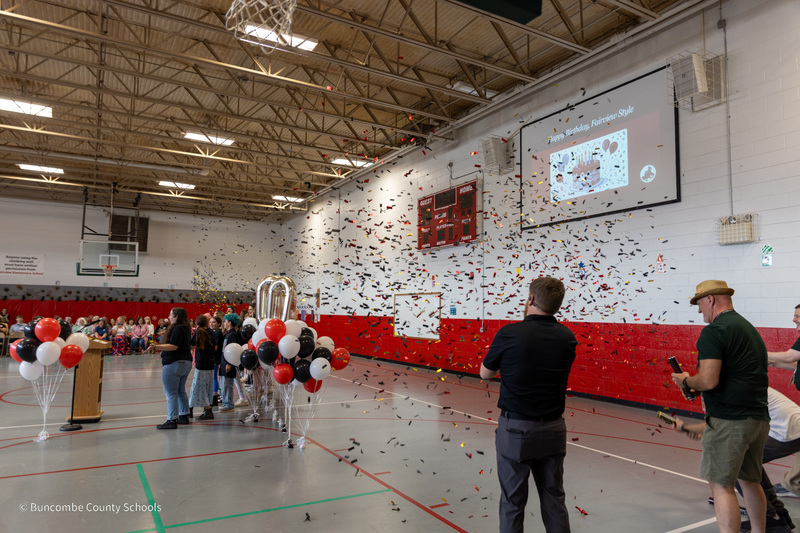 Confetti cannons shoot colorful papers toward speakers in the Fairview gym