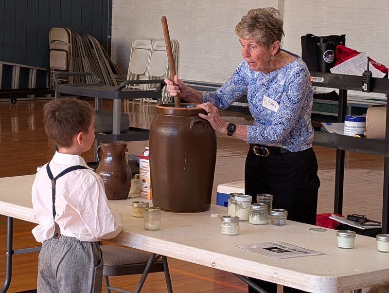 A school visitor shows a boy how a butter churn works.