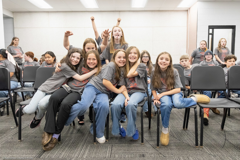 A group of elementary/intermediate students hug and smile while posing for a photo.