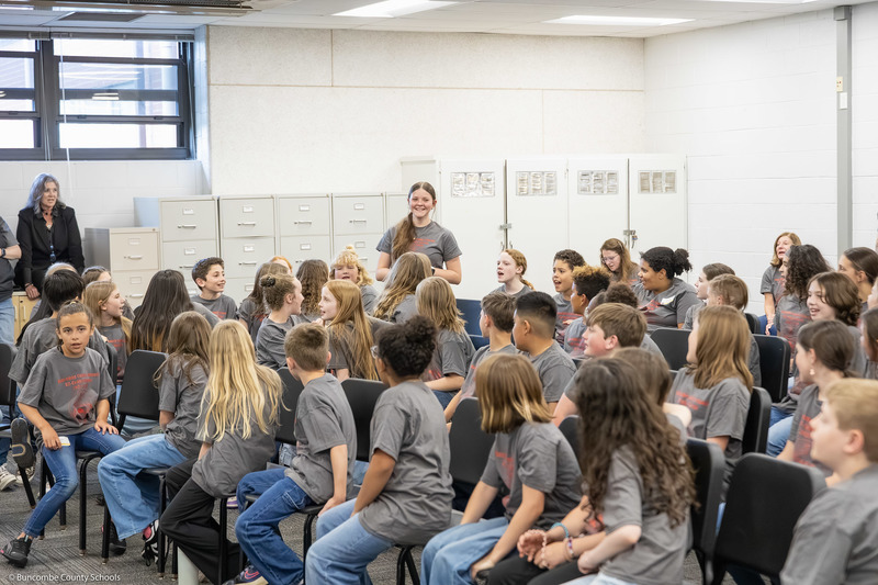 Elementary and Intermediate All-County Chorus students cheer for one student, standing, for an announcement of her birthday.
