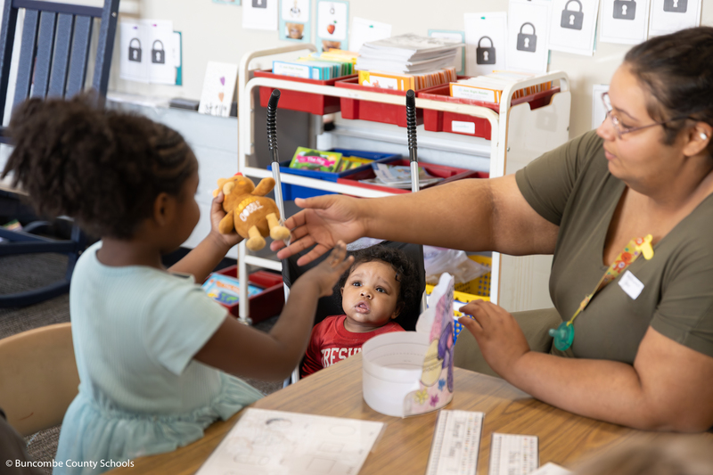 Baby sitting a stroller looking up at her sister.