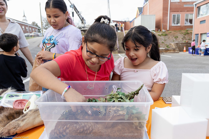 Two students smile as they reach in to touch a turtle.