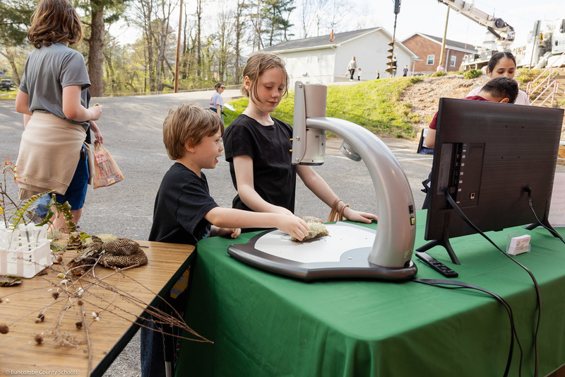 Two students look at a turtle shell under a magnifying scope.