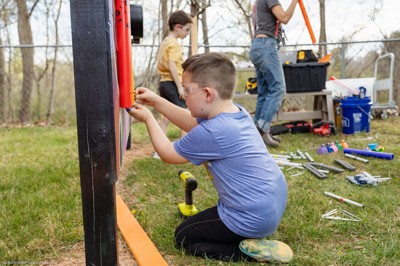 A student drills a plastic tube into a music wall.