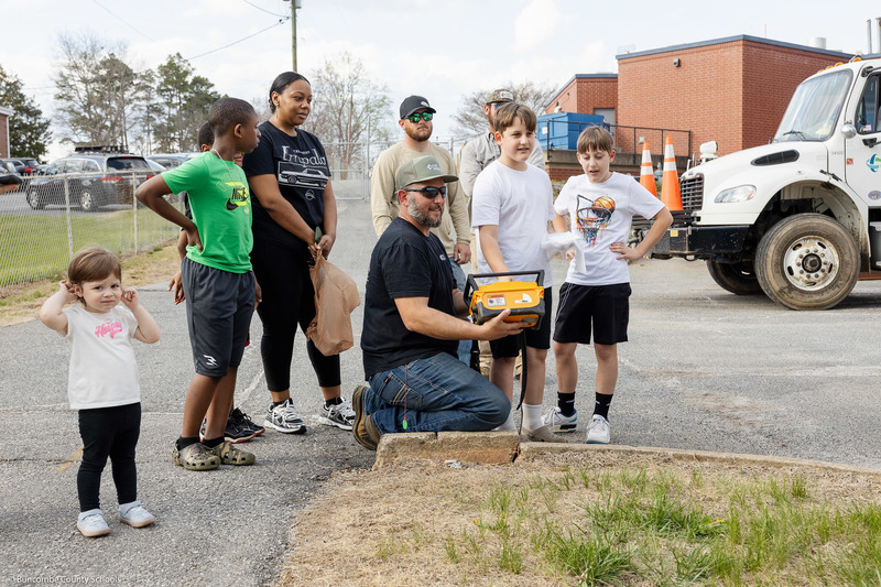 Students and parents watch as a Duke Energy representative operates a truck.