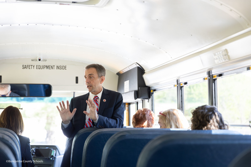 Dr. Jackson at the front of the school bus speaking to the passengers.