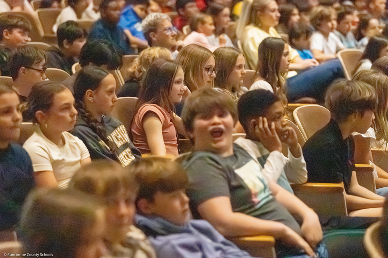 Students, sitting in rows,  listen to the performance.
