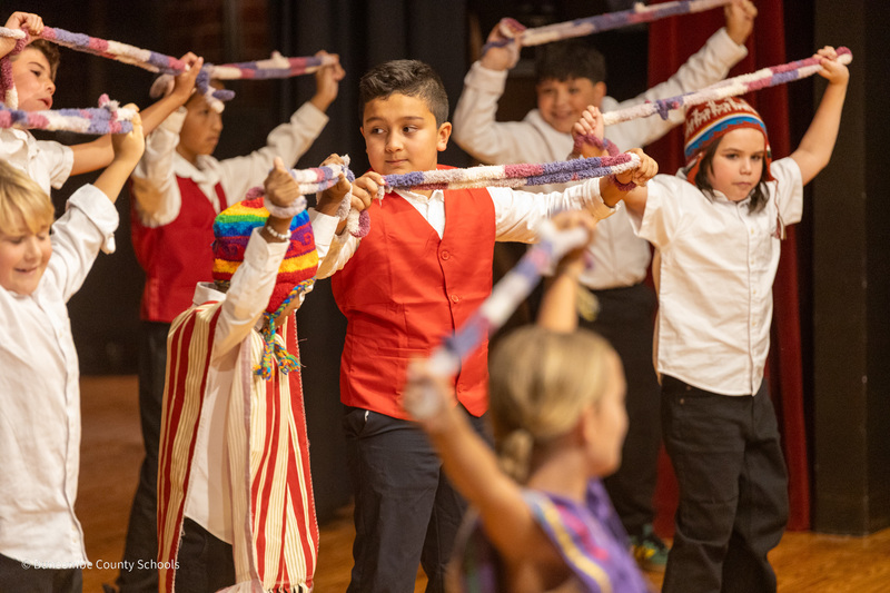 A boy in a red vest holds a colorful cloth that he spins while he dances.