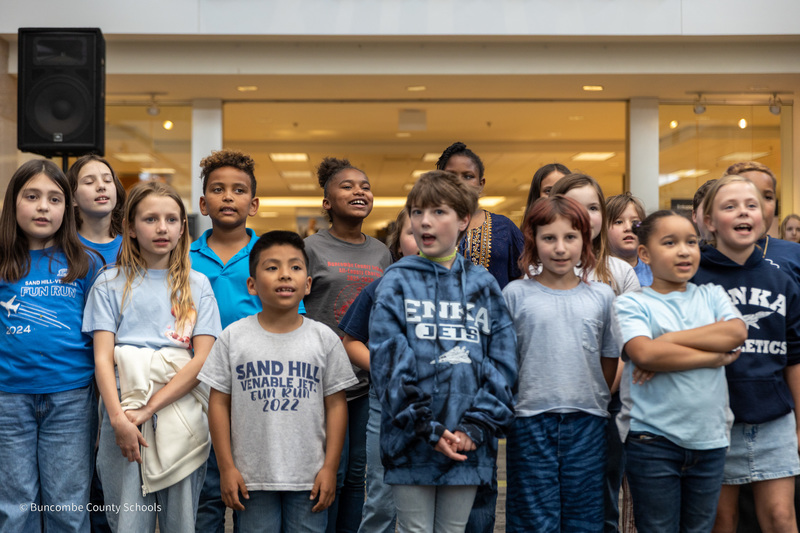 Two rows of students from Sand Hill-Venable Elementary stand and sing in the mall.