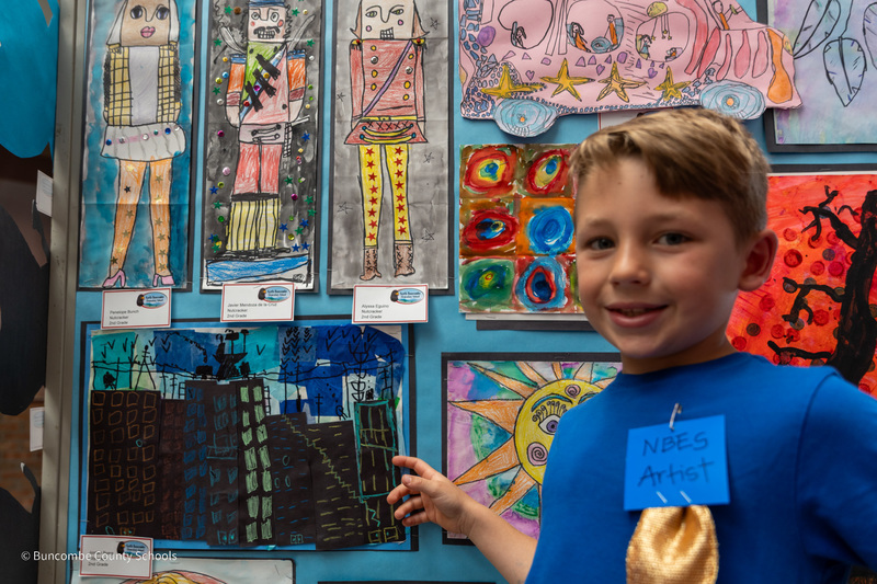 A student points to his artwork of a city skyline.