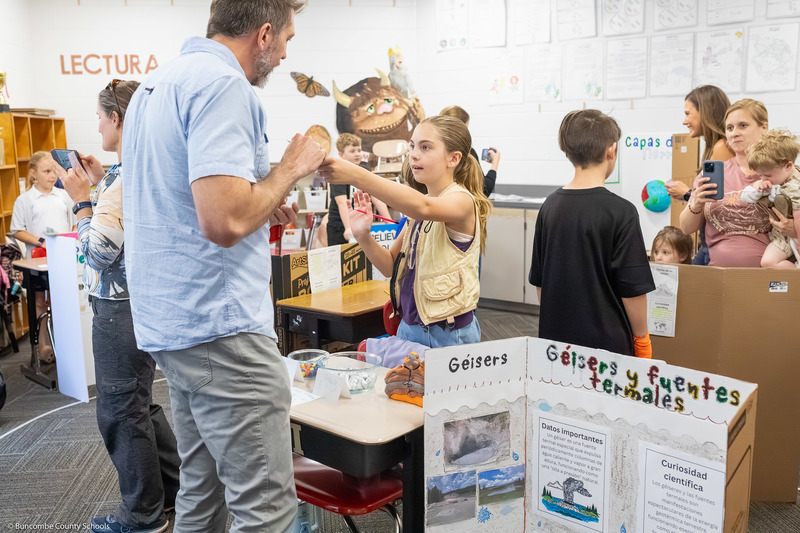 A girl hands an object to a man during her presentation.