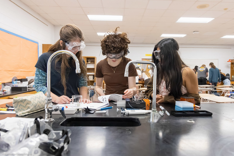 Three students, wearing safety goggles, work on a DNA test.