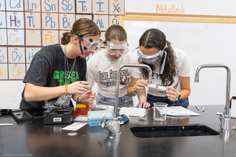 Three students, wearing safety goggles, work on a DNA test.