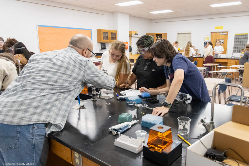 Ryan Smith and three students lean over a table to work on a project.