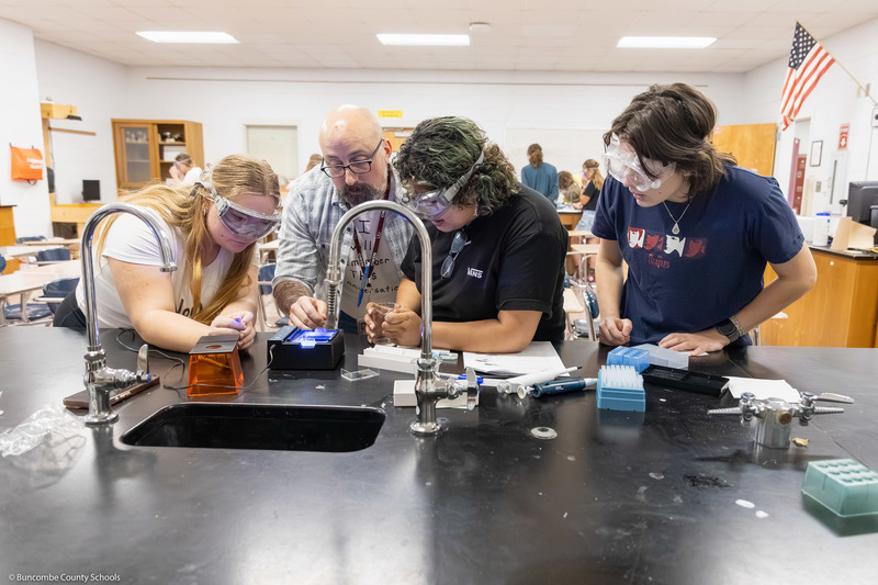 Ryan Smith and three students lean over a table to work on a project.